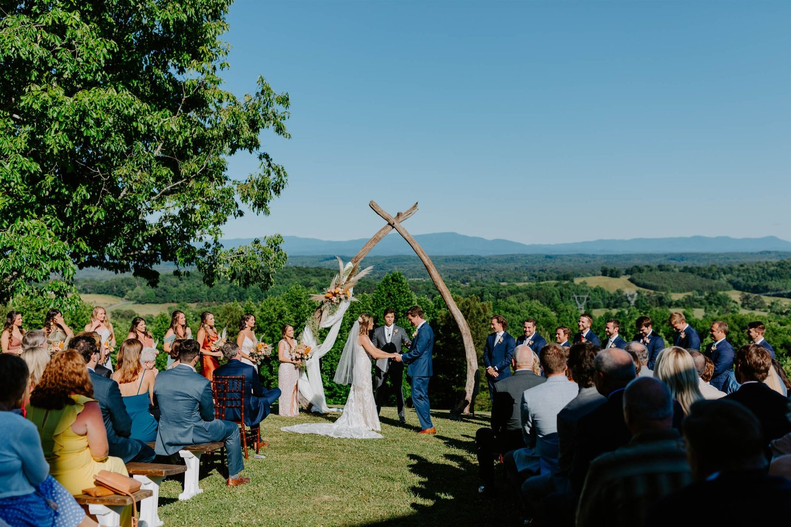 Outdoor wedding ceremony at Chattanooga wedding venue The Views at Sunset Ridge, featuring a rustic wooden arch, panoramic mountain views, and guests gathered under a clear blue sky for a romantic countryside celebration.